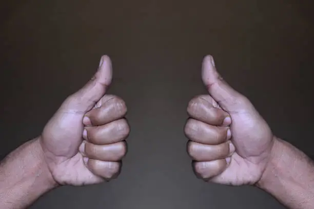 Closeup view of two hands giving both thumbs up as sign of likeness or success. Vertical color photography.
