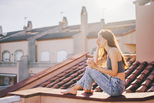 Woman having coffee and enjoying sunny weather on the rooftop terrace