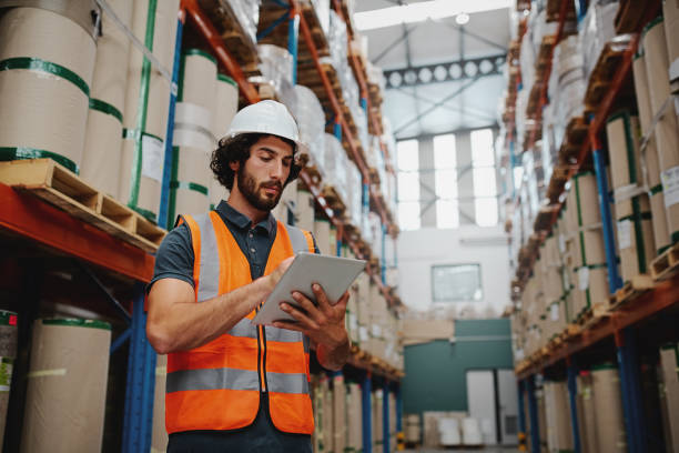 istock Young caucasian engineer in hardhat is using a tablet computer in a heavy industry factory wearing white helmet and orange vest for safety 1207465903