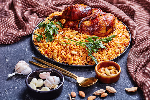 Traditional Saudi Arabian dish chicken and rice kabsa with spices roasted almonds, raisins, and garlic on a black plate on a dark concrete background, horizontal orientation, close-up
