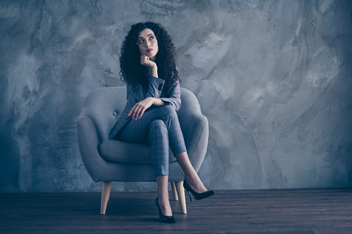 Portrait of her she nice-looking attractive charming classy minded wavy-haired girl psychologist, sitting in chair crossed legs thinking about finance invest gray concrete wall background