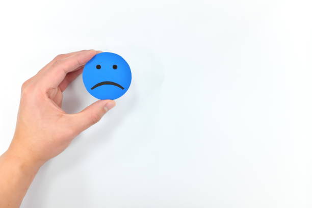 istock Hand holding a blue sad face in white background. Bad customer service, feedback and review. Loneliness concept 1207473174