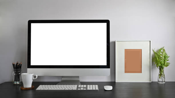 istock Personal workspace computer with blank screen, pencil holder, picture frame, potted plant, and coffee cup putting together on modern wooden table with white wall as background. 1207479160