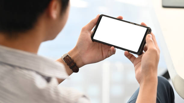 hombre creativo relajante / viendo una película de negro recortado smartphone con pantalla en blanco en blanco en la mesa de trabajo moderna como fondo. relajante después de terminar el concepto de trabajo. - horizontal fotografías e imágenes de stock