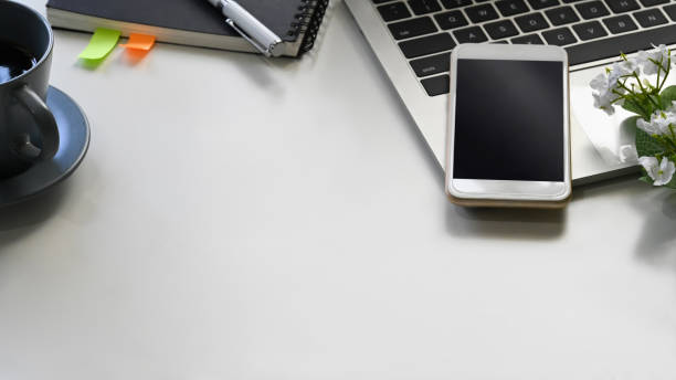 istock Close up image of white working table with accessories putting on it. Flat lay Computer laptop, Coffee cup, Smart phone with black blank screen, Notebook. Modern and Orderly style workplace concept. 1207479365