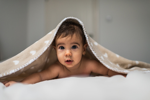 Cute baby girl in bed under a fluffy blanket.