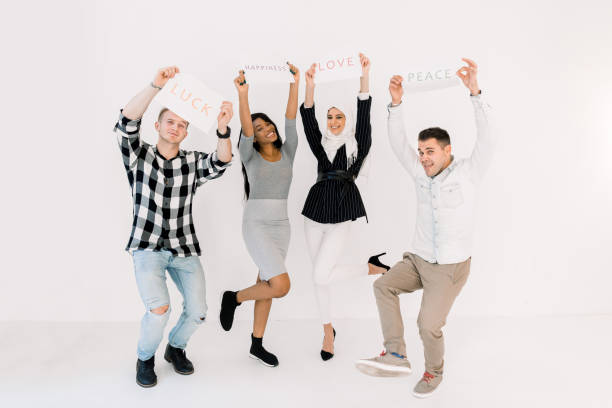 istock Four multiethnical young smiling people with placards and posters about love, peace and happiness, posing on white background. Social slogans, international frienship concept 1207487136