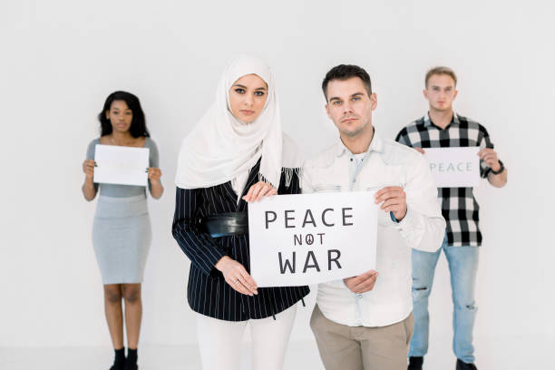 若い抗議者、イスラム教徒の女性と白人の男性は、戦争のスローガンでポスターを保持し、平和を救うために唱えます。アフリカの女性と白人の男性は、背景に平和のスローガンを持ってい� - currency silence censorship behavior ストックフォトと画像