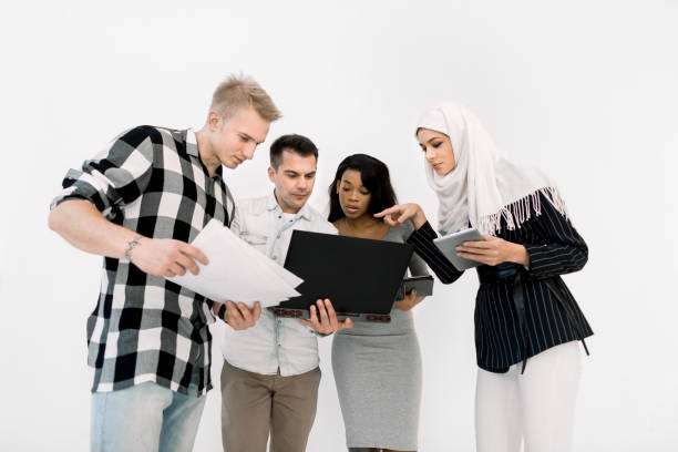 istock Four young people studying, multi-ethnic beautiful women and men working together and using laptop and tablet, wearing casual clothes, standing over white background 1207487165