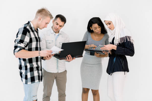istock Group Of Four Multi Ethnic Students, working studying together, using laptop and tablet, standing On White Background. International business, education concept 1207487403
