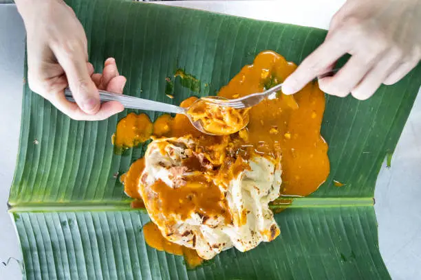 Photo of Person eating roti canai or paratha with curry on banana leaf, favourite Malaysian food