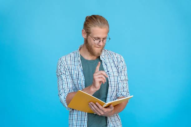 Young thoughtful man student hipster inspired writer hold pen pencil hand have idea think plan make notes fill in diary schedule write novel look at journal isolated studio background copy space