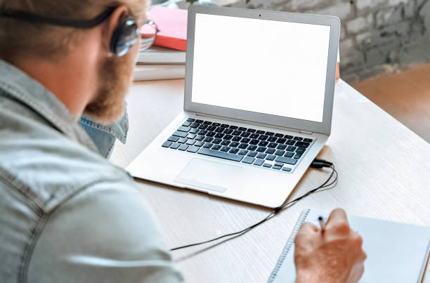 au-dessus de l’épaule près vers le haut de l’homme l’étudiant portent des écouteurs emploient l’étude d’ordinateur portable en ligne écoutent le cours de formation de montre de prendre des notes e apprenant l’appel d’appel de skype maqu - application form audio photos et images de collection