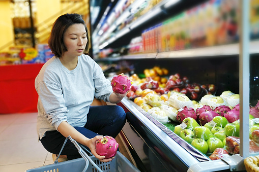 A woman is selecting fresh fruits such as dragon fruit in supermarket.