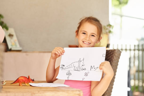 Look at my cute dinosaurs Shot of a innocent little girl showing her drawing of a dinosaurs dinosaur drawing stock pictures, royalty-free photos & images