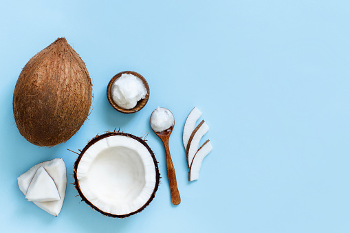 Coconut oil in a bowl with a spoon and coconut pieces top view on a blue background