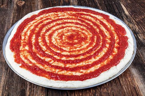 Close-up of Italian pizza preparation. Spreading tomato sauce on pizza dough and preparing for baking with other ingredients.