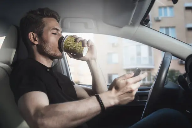 Photo of Male sitting in the car hold coffee and phone