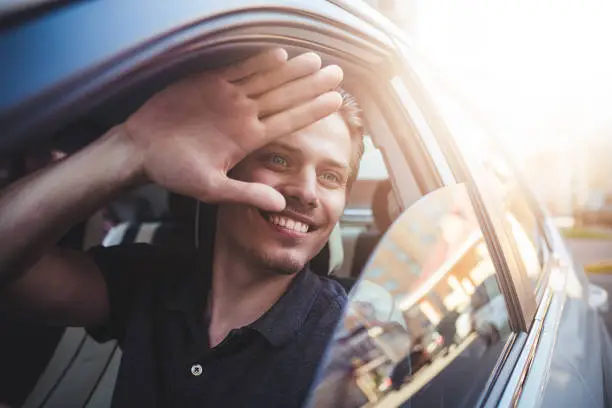 Photo of Say hello. Close up side portrait of happy caucasian man driving car.