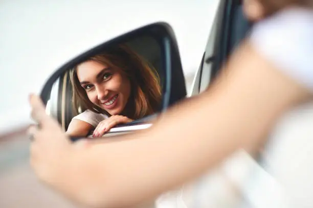 Photo of Portrait of cute smiling girl sit in the car and look at the car mirror