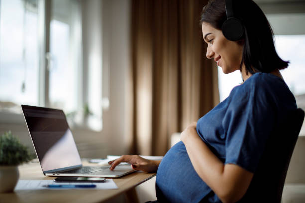 mujer embarazada con auriculares usando portátil - mothers audio fotografías e imágenes de stock