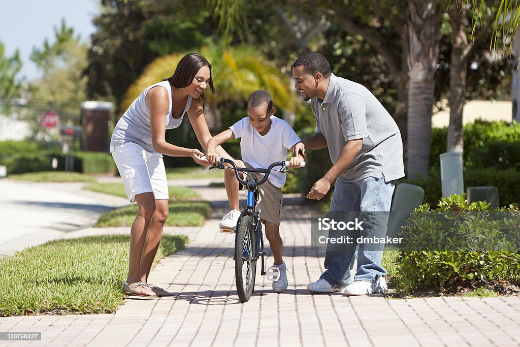 African American Family WIth Boy Riding Bike & Happy Parents A young African American family with boy child riding his bicycle and his happy excited parents encouraging him. Boys Stock Photo