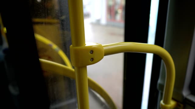 The bus doors close and the bus pulls away from the stop. Close-up of the yellow handrail. View from inside the bus. Blurred background. 4K