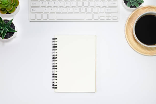 istock Workspace, White office desk table. View from above with keyboard, notebooks and white cup of black coffee on wooden plate. Top view, flat lay with copy space. Business concept. 1207508993