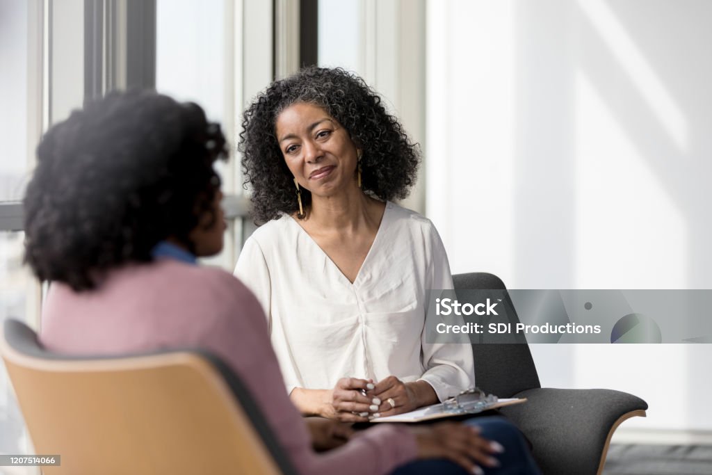 Mature counselor listens compassionately to unrecognizable female client The mature adult female therapist listens compassionately to the unrecognizable female client share her problems. Mental Health Professional Stock Photo