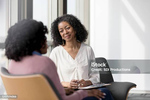 Mature Counselor Listens Compassionately To Unrecognizable Female Client Stock Photo - Download Image Now