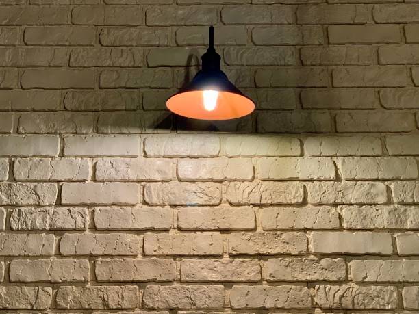 istock Large black lamp on a background of a white brick wall. A light bulb illuminates a white brick wall. 1207514456