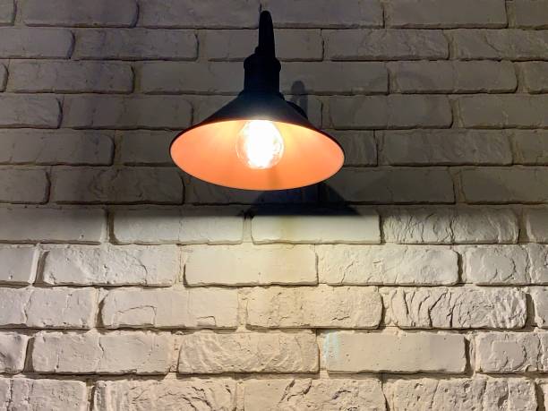 istock Large black lamp on a background of a white brick wall. A light bulb illuminates a white brick wall. 1207515054