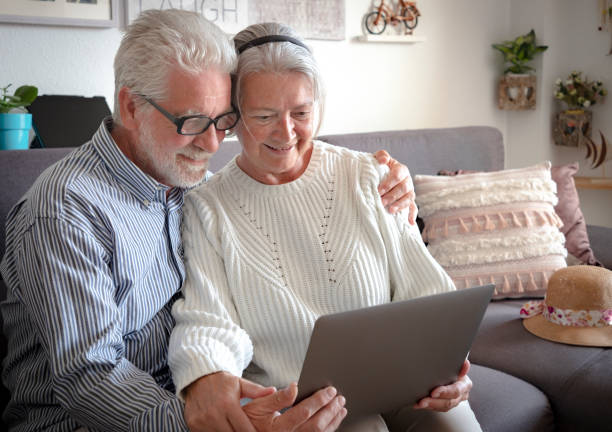 istock Elderly web surfer. Two smiling senior people sharing and looking at laptop and planning a new travel. White hair - couple in retirement 1207515947