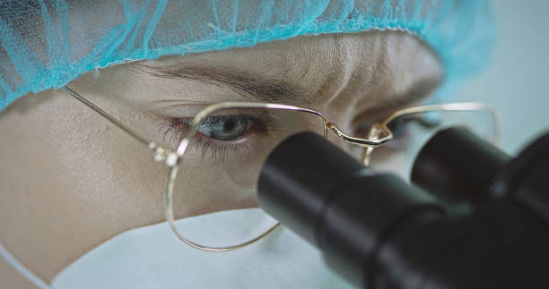 istock Woman in eyeglasses and hospital cap looking through a microscope 1207517306
