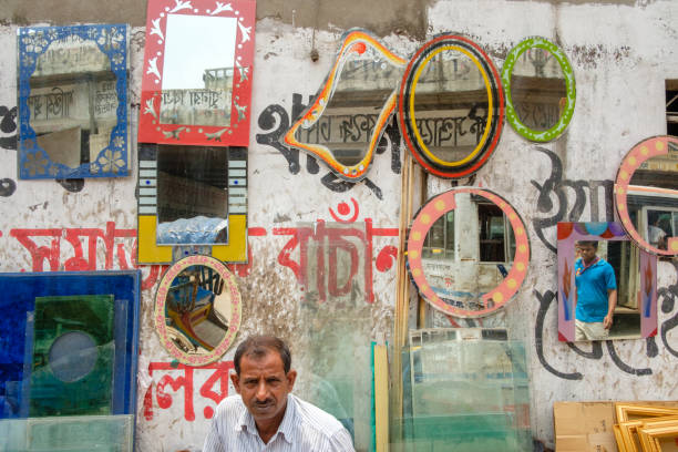 Dhaka, Bangladesh - May 15, 2017: Man sells mirrors hanging on a street wall at Dhaka’s Babu Bazar.