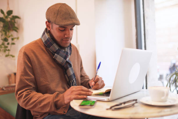 One young Afro-American hipster man writing in a note pad some ideas.
