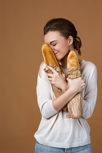 Portrait of beautiful smiling young woman holding paper bag with bread on studio yellow background. girl smells the smell of fresh fragrant long loaf