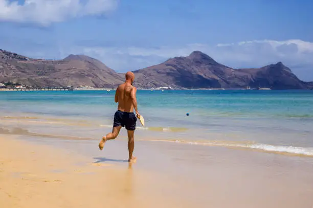 Man running after a ball while playing racketball at the beach in Porto Santo island