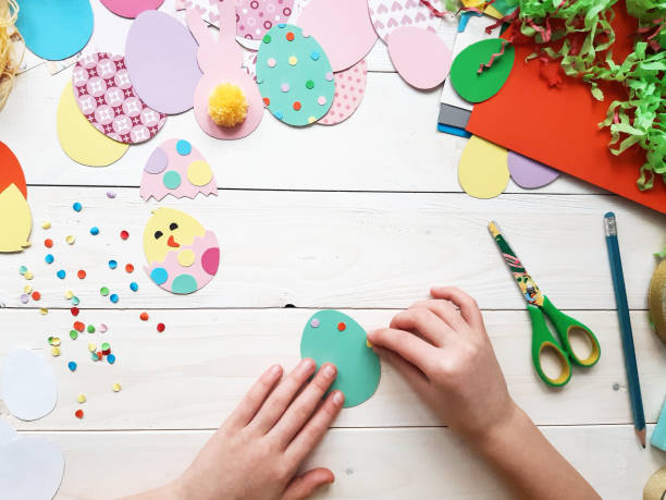 istock The child makes crafts with his own hands for the Easter. Colorful handmade from multi-colored paper. Scissors, cardboard, eggs, chicken, rabbit. Art creativity on a wooden table. Top view, copy space 1207541460