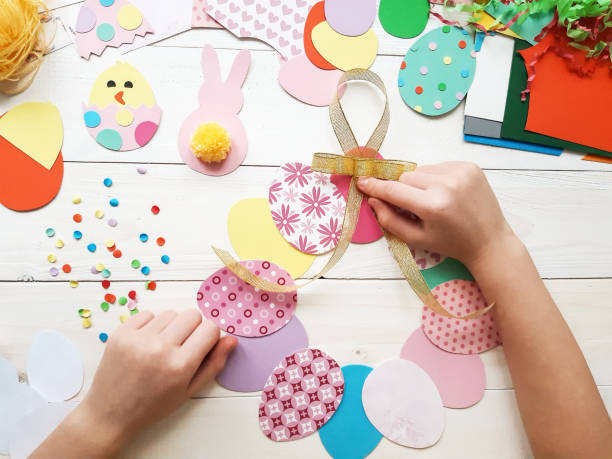 istock The child makes crafts with his own hands for the Easter. Colorful handmade from multi-colored paper. Scissors, cardboard, eggs, chicken, rabbit. Art creativity on a wooden table. Top view, copy space 1207541995