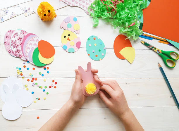istock The child makes crafts with his own hands for the Easter. Colorful handmade from multi-colored paper. Scissors, cardboard, eggs, chicken, rabbit. Art creativity on a wooden table. Top view, copy space 1207542027