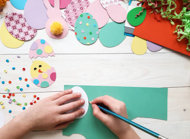 istock The child makes crafts with his own hands for the Easter. Colorful handmade from multi-colored paper. Scissors, cardboard, eggs, chicken, rabbit. Art creativity on a wooden table. Top view, copy space 1207542050