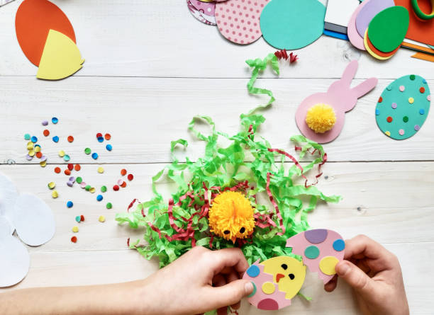 istock The child makes crafts with his own hands for the Easter. Colorful handmade from multi-colored paper. Scissors, cardboard, eggs, chicken, rabbit. Art creativity on a wooden table. Top view, copy space 1207542156