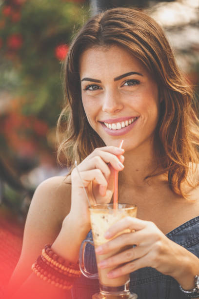 istock Smiling woman taking a sip of coffee while looking at camera 1207543840