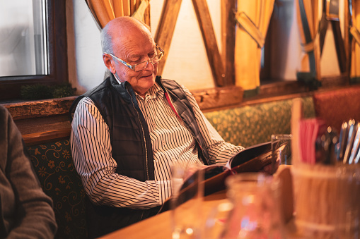 senior man reading menu in rustic alpine restaurant in european mountains ski resort during winter vacations