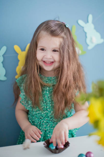 istock Toddler girl play with easter eggs. Spring easter decorations, bunny garland, flowers on blue background. 1207547356