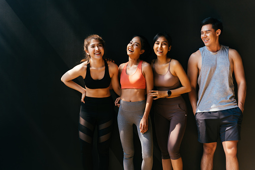 Happy smiling man and women having fun talking in gym. Group of young people relaxing in gym after workout training with black background.