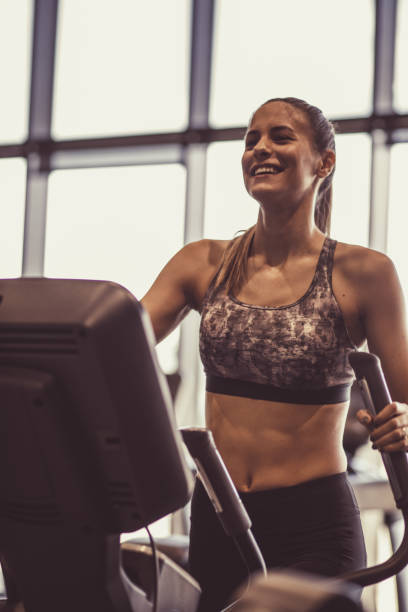 istock Smiling female athlete doing a warm up on a exercise machine at the gym 1207548123