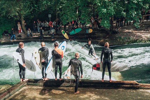 Munich, Germany - September 20, 2019: Surfers practice in Englischer Garden in Munich on the artificial wave at Eisbach, small river crossing the park, a lot of people are watching, other surfers are waiting for their ride.