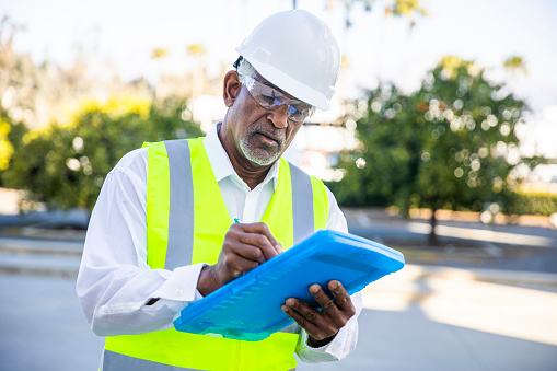 A senior black male construction site manager visually inspects a building project